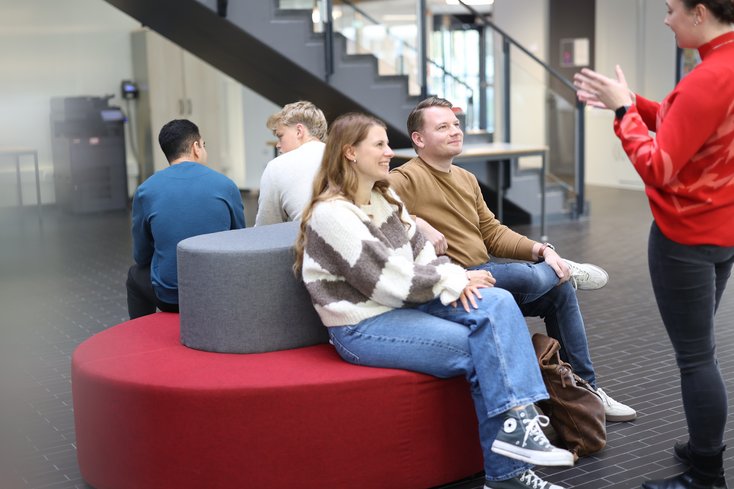Studierende sitzen auf den Sofas im Lichthof der Hochschule und bekommen etwas erklärt