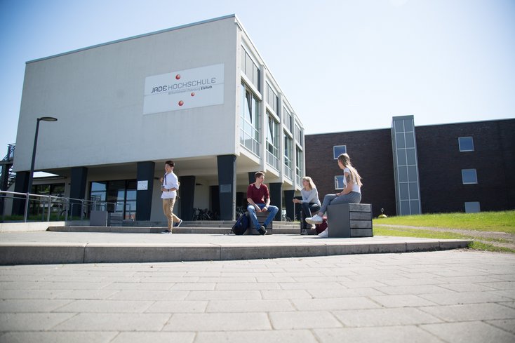 Studierende sitzen bzw. stehen vor dem Hochschulgebäude