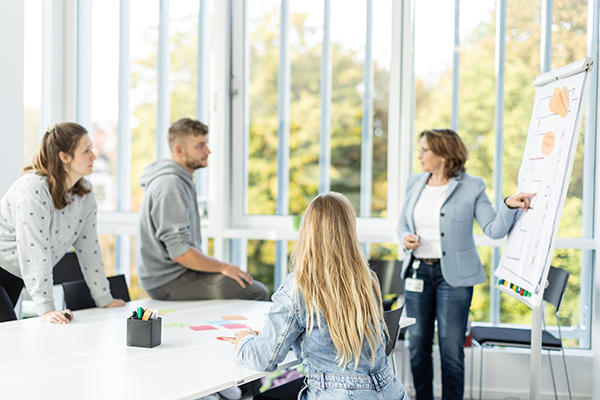 Dozentin zeigt auf Flipchart und spricht mit Studierenden