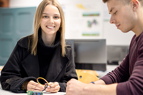 Studentin hält Elektronikteile in der Hand und lächelt in die Kamera